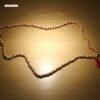 Lifestyle product photo of MalaMantra Red String Mala on a neutral-toned surface.