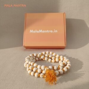 MalaMantra 108 bead Tulsi wood Jaap Mala with saffron orange string and tassel, photographed on a neutral-toned linen surface.